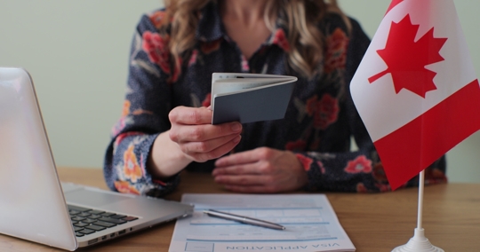 Woman looking at immigration papers next to Canadian flag
